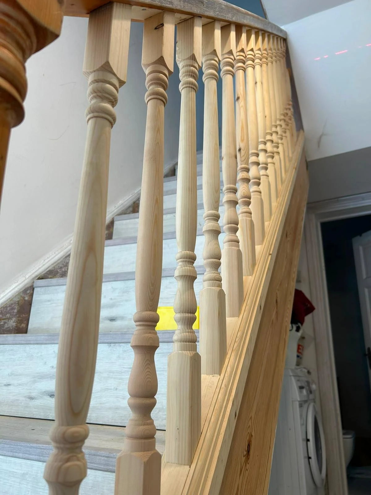 Close-up view of a wooden staircase railing with turned vertical balusters and light-colored steps in a residential interior.