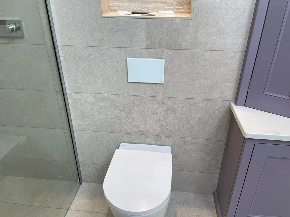 Modern white toilet against tiled wall with recessed shelf and purple cabinet beside it.