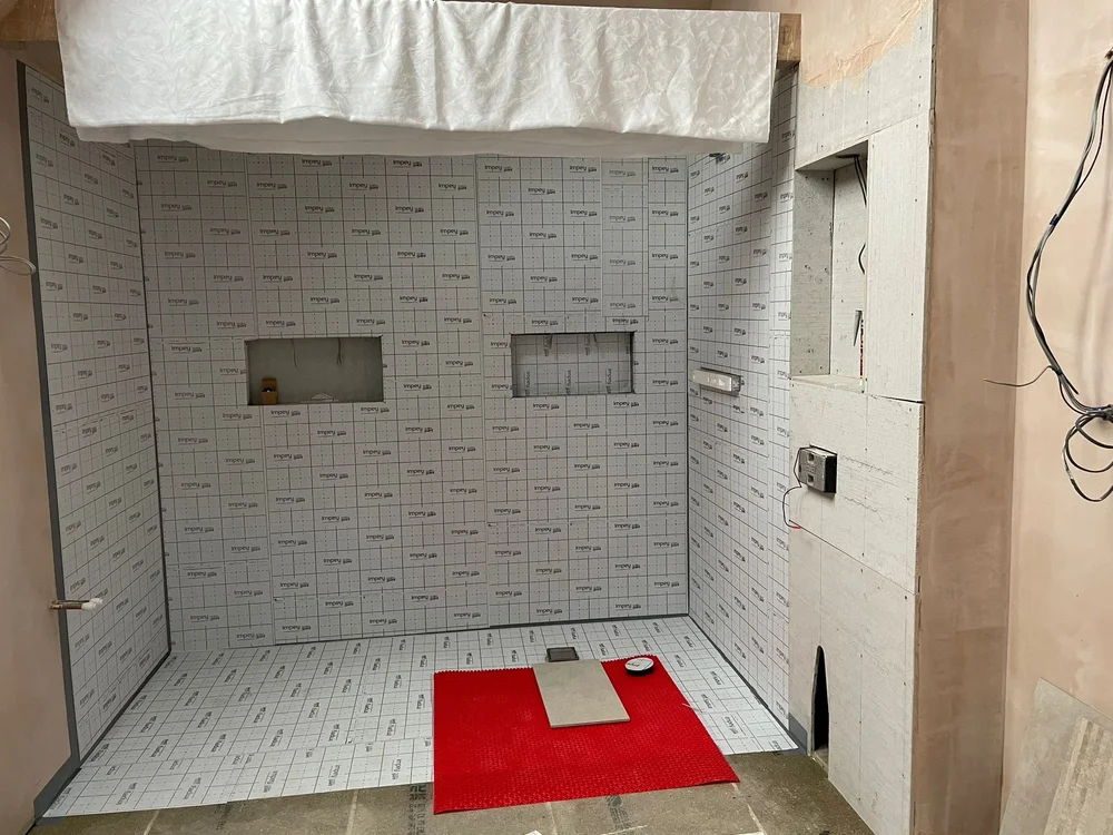 Unfinished shower area with waterproof wall panels and a red mat on the floor during construction.