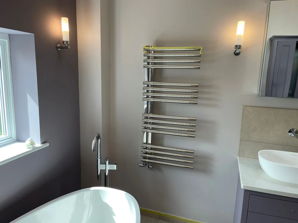 Modern bathroom with white tub, chrome towel radiator, wall sconces, and a vanity with vessel sink.