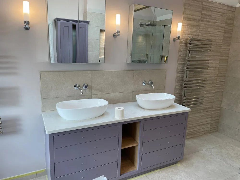 Modern bathroom vanity with double white vessel sinks, mirrors, and purple drawers under a marble countertop.