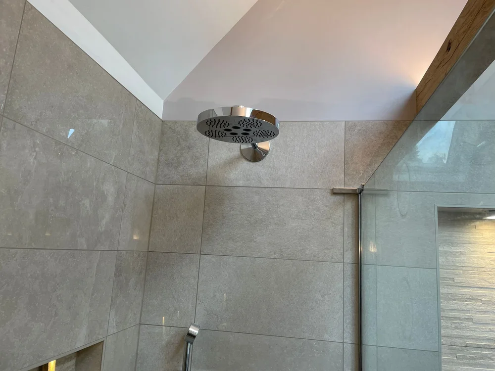 Modern showerhead mounted on a tiled shower wall with glass door and recessed shelf.