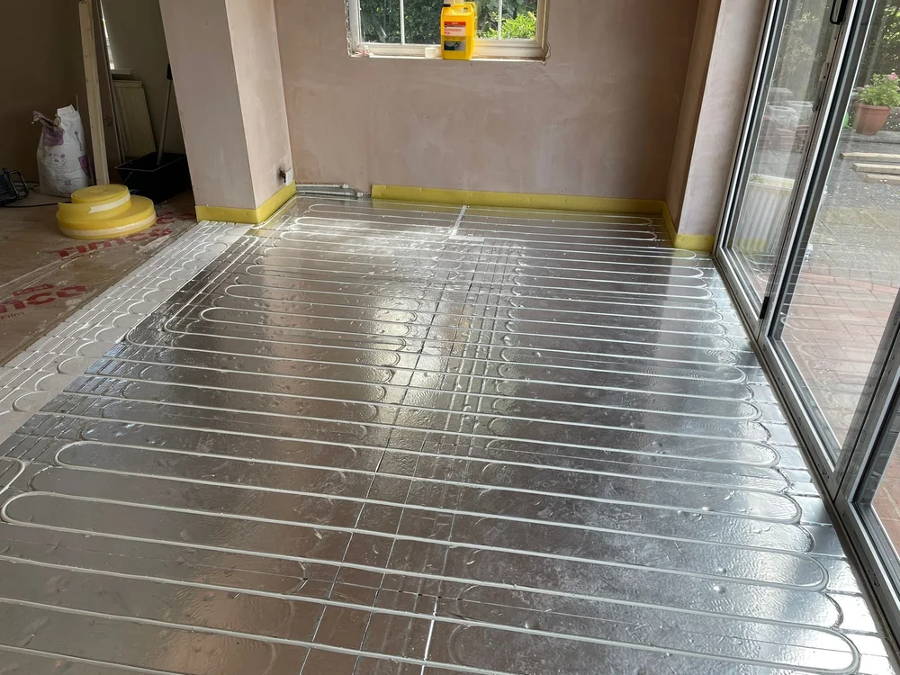 Installation of underfloor heating pipes laid out in a room with large glass doors and a window.