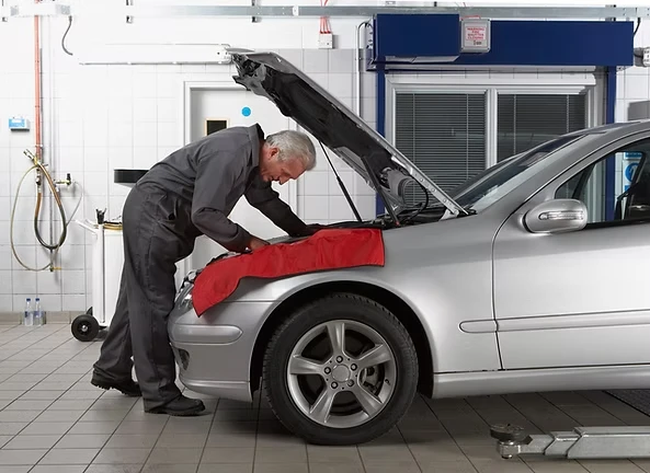 Mechanic servicing a car with the bonnet up and a cover.