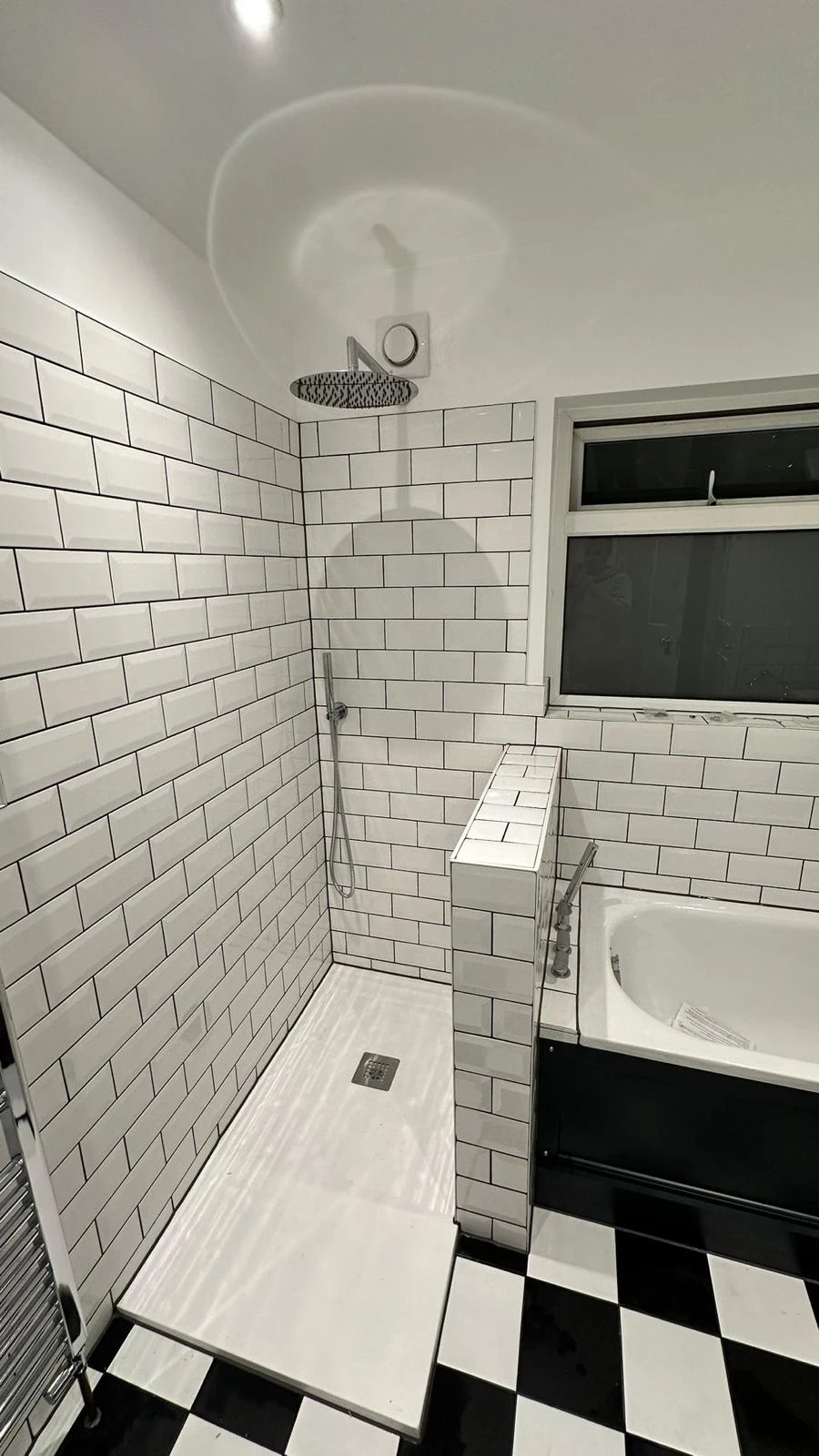 Modern bathroom featuring a walk-in shower with subway tiles, a bathtub, and black-and-white checkered flooring.
