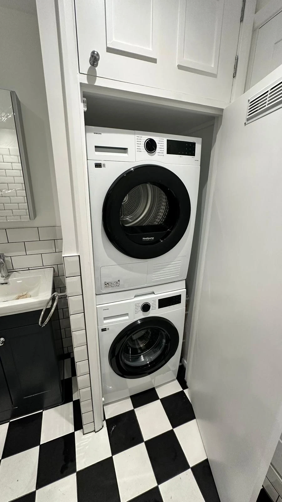 Compact laundry area featuring a stacked washer and dryer, a sink, and a black and white checkered floor.