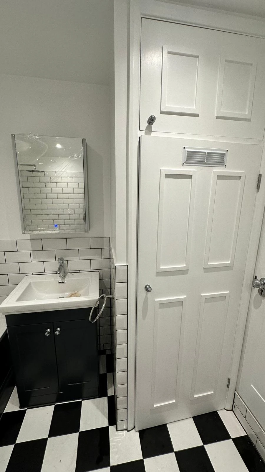 Modern bathroom featuring a black and white tiled floor, a sleek sink, a rectangular mirror, and a white door.