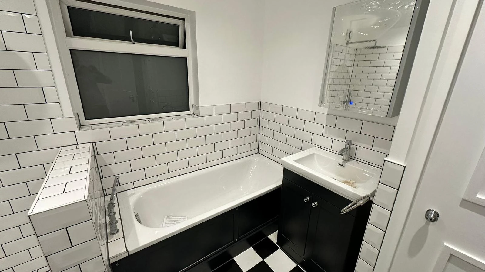 Modern bathroom featuring a white bathtub, black cabinetry, and tiled walls with a window and mirror.