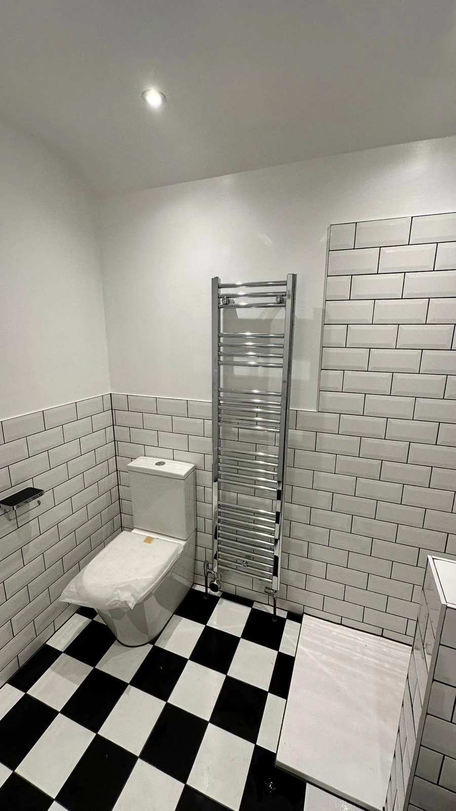 Modern bathroom featuring black and white tiled floor, white toilet, chrome towel radiator, and minimalist design.