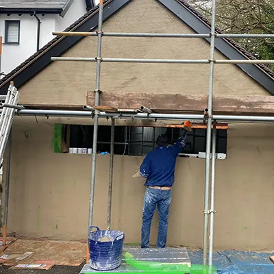 A man standing on scaffolding in front of a house.