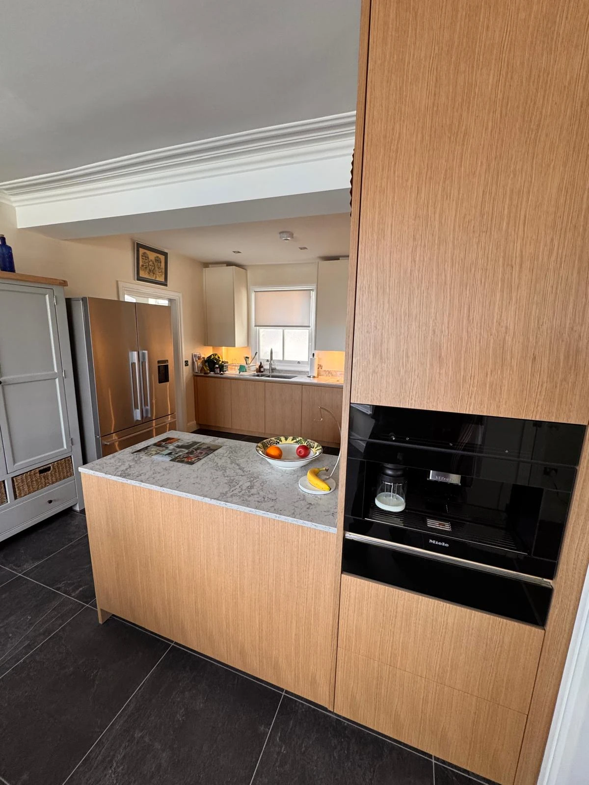 Modern kitchen featuring wood cabinetry, a gray countertop with fruit bowl, and built-in appliances. Sleek black and light decor.