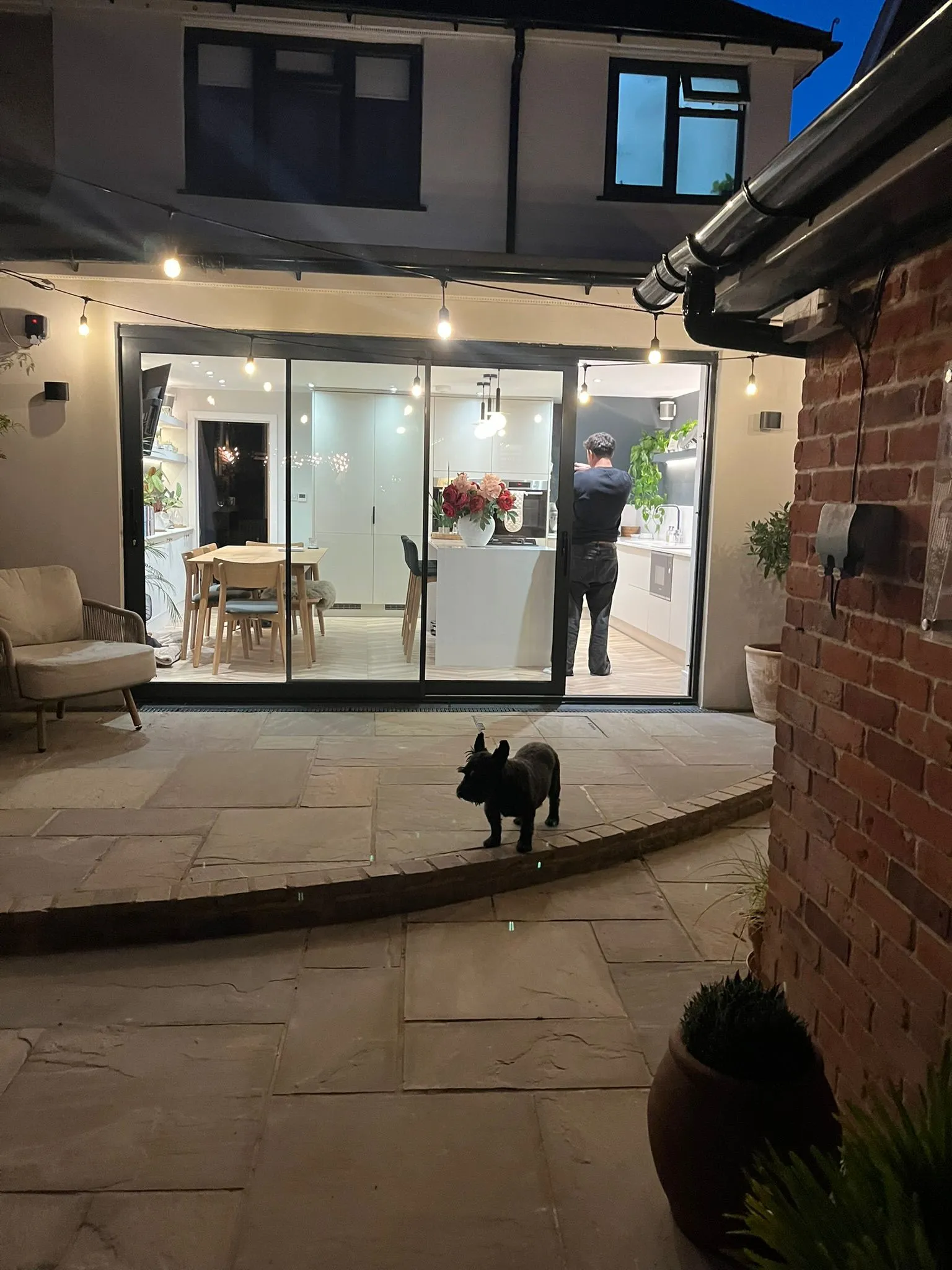 A man standing outside of a house with a dog.
