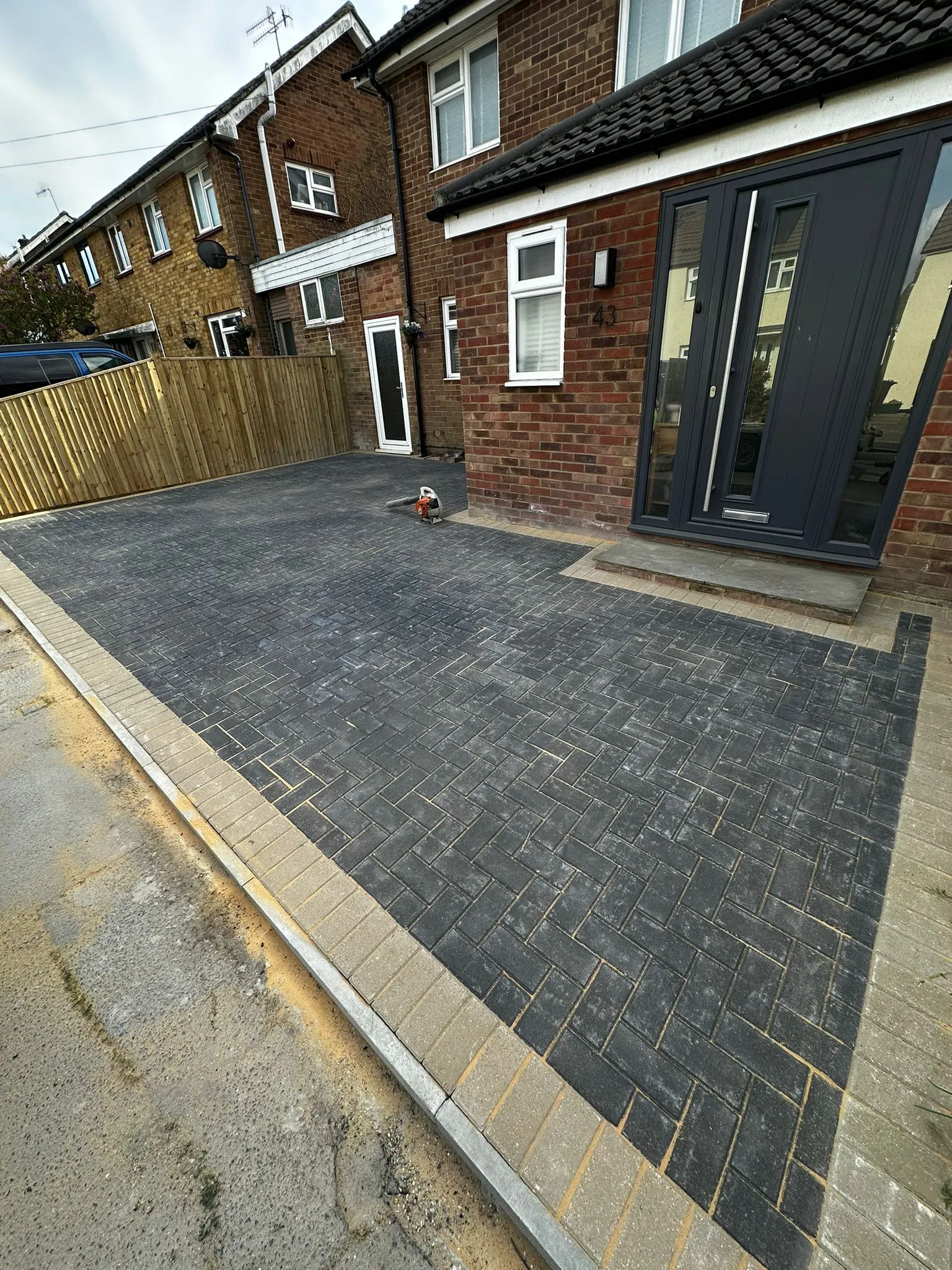 A brick paved driveway with a wooden fence in the background.