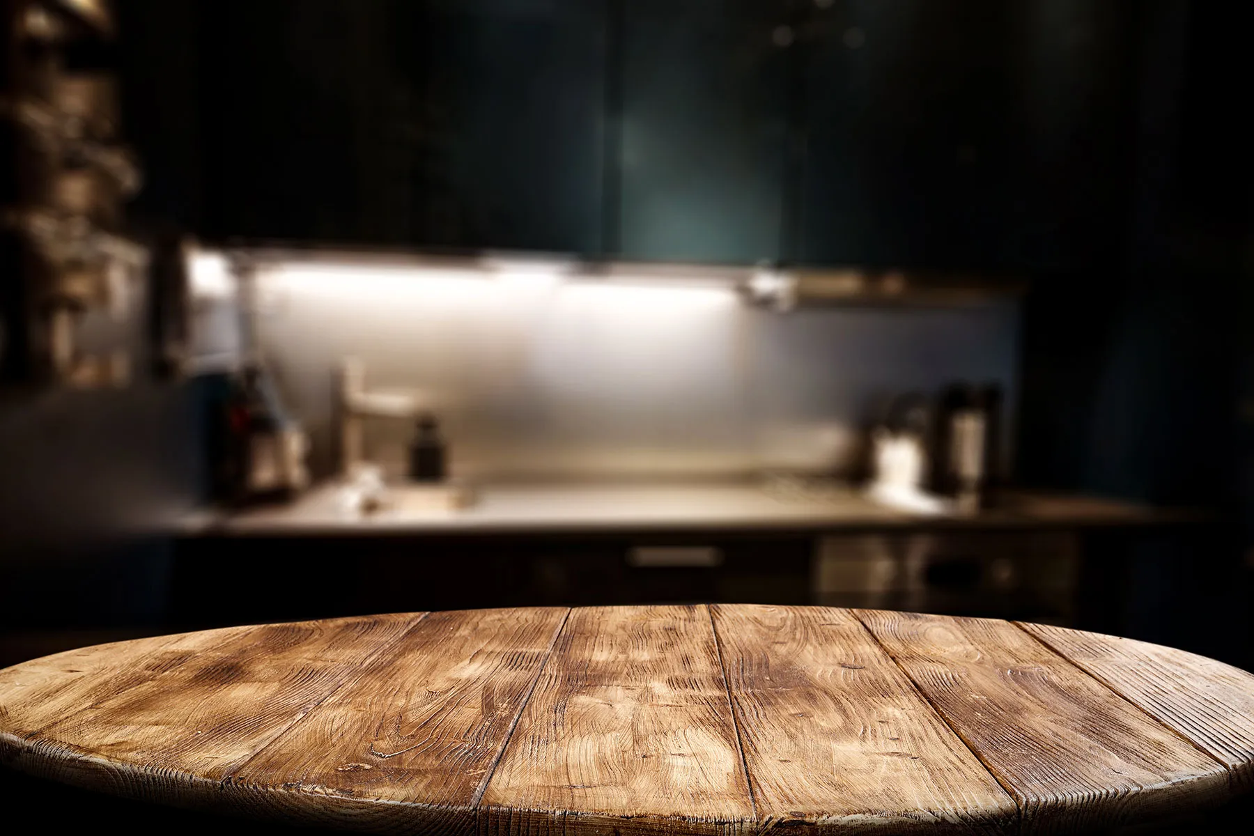 A wooden table top in a kitchen with a sink.